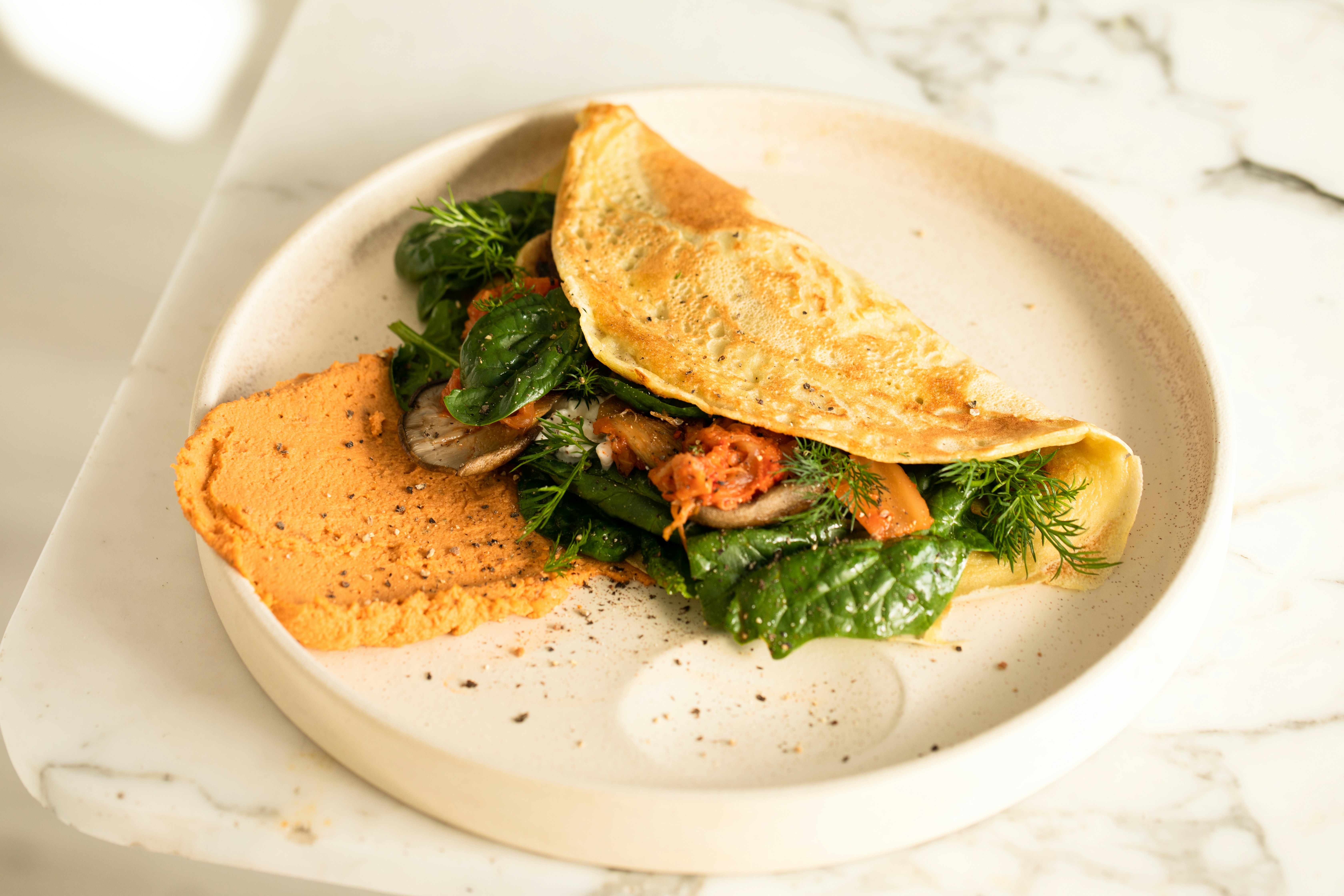 White plate topped with an omelet and
          greens